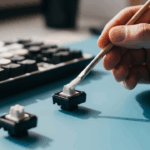 A close-up image of a person carefully applying lubricant to a keyboard stabilizer component with a small brush, illustrating the process of keyboard tuning.